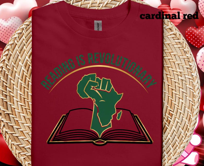 May include: A cardinal red t-shirt with the words "READING IS REVOLUTIONARY" in gold and green. The design includes a green fist and the African continent above an open book.