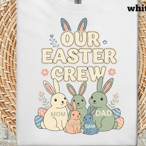 Op de afbeelding: Wit T-shirt met een afbeelding van een paashaasfamilie en de tekst "OUR EASTER CREW". Het ontwerp maakt gebruik van pastelkleuren en bloemaccenten, met de woorden "MOM", "DAD", "LIAM" en "SAM" onder de konijnen.