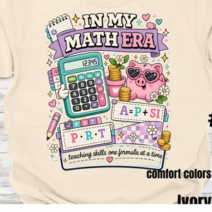May include: An ivory t-shirt featuring a colorful graphic with the text IN MY MATH ERA and teaching skills one formula at a time. The design includes a teal calculator, a pink piggy bank with heart sunglasses, gold coins, and math formulas.