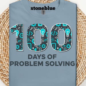 May include: A light blue t-shirt with the text "stoneblue" at the top. The shirt features the number "100" in a teal and white design, with the words "DAYS OF PROBLEM SOLVING" below.