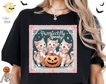 Puede incluir: Camiseta negra con un diseño de Halloween. El gráfico muestra tres gatitos con lazos rosas, una calabaza tallada y el texto "Purrfectly Spooky" dentro de un marco decorativo. También se representan murciélagos y una luna.