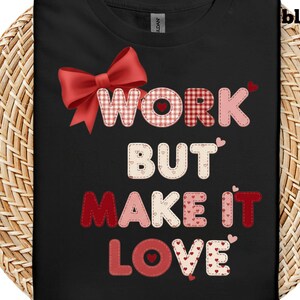 以下が含まれることがあります： 黒いTシャツに「WORK BUT MAKE IT LOVE」の文字が赤とピンクのパッチワークでデザインされています。赤いリボンとハートがデザインを飾り、バレンタインデーをテーマにしています。