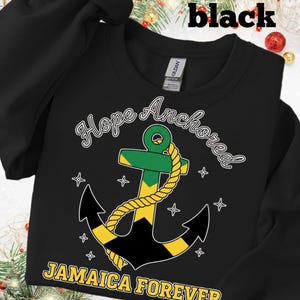 Puede incluir: Sudadera negra con el texto "Hope Anchored" y "Jamaica Forever". El diseño presenta un ancla con los colores de la bandera jamaicana y una cuerda amarilla. La sudadera es de la marca Gildan.