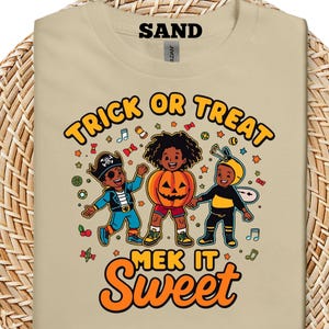 Puede incluir: Camiseta color arena con un diseño de Halloween. El diseño presenta a tres niños disfrazados: un pirata, una calabaza y una abeja. El texto "Trick or Treat" y "Make it Sweet" está en naranja y amarillo.