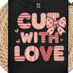 Puede incluir: Camiseta negra con la frase "CUT WITH LOVE" en un diseño de patchwork. Las letras son en tonos rosa y rojo, con motivos de corazones y tijeras. También hay un gran lazo decorado con corazones.