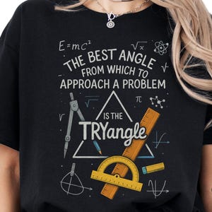 May include: Black t-shirt featuring a maths-themed design. The graphic includes equations, a compass, protractor, and the text "THE BEST ANGLE FROM WHICH TO APPROACH A PROBLEM IS THE TRYangle."