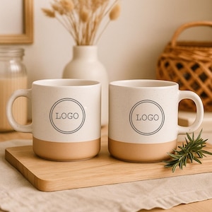 May include: Two speckled ceramic mugs with a tan base and a white upper section. Each mug has a handle and a circular logo that says "LOGO". The mugs are on a wooden cutting board.