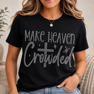 Może przedstawiać: Czarny t-shirt z krótkim rękawem z napisem "MAKE HEAVEN CROWDED" wykonanym ze srebrnych dżetów. Wzór zawiera krzyż z dżetów umieszczony między słowami oraz małe akcenty w kształcie gwiazdek z dżetów rozmieszczone na całej grafice.