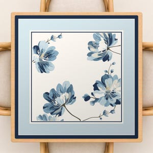 May include: Square framed artwork featuring a floral design. The artwork has a light blue border and a dark blue frame. The floral design features blue flowers with white accents on a white background. The artwork is displayed on a light wood frame.
