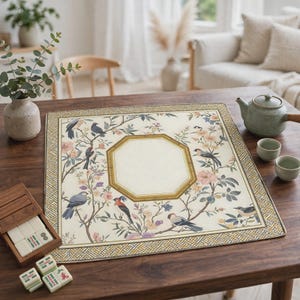 May include: A square mahjong mat featuring a cream-coloured surface with a central octagonal border, surrounded by illustrations of various birds perched on flowering branches. The mat has a geometric patterned border in shades of gold and brown.
