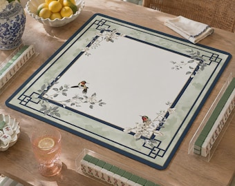 May include: A square mahjong mat featuring a cream-colored center with illustrations of two hummingbirds and floral branches. The mat has a wide sage green border with a dark blue geometric frame and corner accents, providing a flat surface.