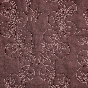 May include: A close-up of a maroon fabric with a repeating pattern of white stitched botanical designs. The design features circular shapes with leaf-like details and star-shaped elements, creating a textured surface.