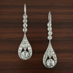 May include: A pair of elegant drop earrings. Each earring features a series of small, round, clear gemstones leading to a teardrop-shaped design. The teardrop is encrusted with smaller gemstones, culminating in a larger, round gemstone at the bottom.