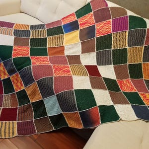 May include: A handmade patchwork blanket with a variety of colors and textures. The blanket is made of squares in shades of green, brown, red, purple, and white. The blanket is draped over a white sofa.