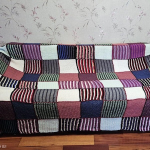 May include: A colorful, patchwork-style sofa. The sofa is covered in a knitted blanket with a variety of colors, including purple, blue, green, red, and white. The design is a mix of solid squares and striped patterns.