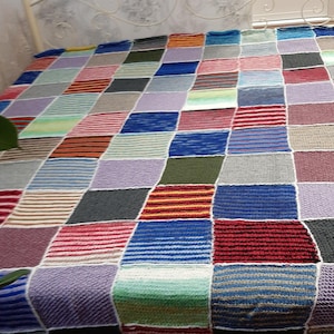 Può includere: Una colorata trapunta patchwork fatta a mano. La trapunta presenta una varietà di quadrati in diversi colori e motivi, tra cui strisce e blocchi pieni. La trapunta è realizzata in filato morbido e strutturato ed è stesa su un letto.