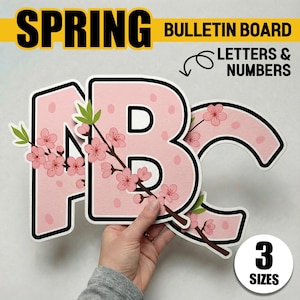 May include: Pink ABC letters with cherry blossom accents for a bulletin board. The letters have a white outline and black border. The word "SPRING" is in large black letters on a yellow banner. The words "BULLETIN BOARD LETTERS & NUMBERS" are also visible.