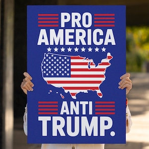 May include: A blue sign with the text "PRO AMERICA" above and "ANTI TRUMP" below. The sign features a map of the United States with the American flag design. The sign is held up by a person.