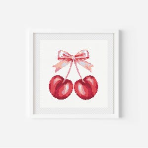 Puede incluir: Dos cerezas rojas con un lazo rosa atado alrededor de sus tallos. Las cerezas están sobre un fondo blanco.