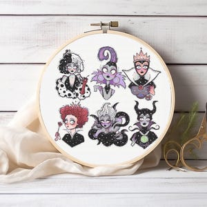 May include: A white embroidery hoop with a white fabric inside. The fabric has six embroidered images of Disney villains, including Cruella de Vil, Maleficent, and Ursula. The villains are all depicted in a cartoon style with black outlines.
