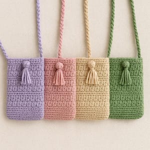May include: Four crochet phone bags in pastel colors: lavender, pink, beige, and green. Each bag has a matching tassel and a braided strap. The bags are rectangular with a textured stitch pattern, perfect for carrying a phone or small items.
