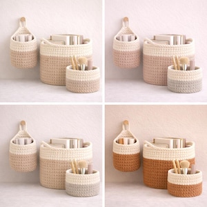 Puede incluir: Un conjunto de cuatro cestas de almacenamiento de ganchillo en varios tamaños y colores. Cada cesta está hecha a mano con un diseño de dos tonos, con una parte superior neutra y una parte inferior de color. El conjunto incluye una cesta colgante, una cesta redonda grande y una cesta redonda pequeña.