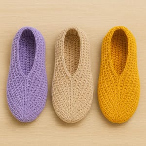 May include: Three knitted slippers in a row, in lavender, beige, and yellow. The slippers are made with a thick yarn and have a simple design. The slippers are ideal for wearing indoors. Each slipper is approximately 25 cm long.