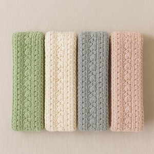 May include: Four rectangular knitted washcloths in shades of green, cream, gray, and pink. Each washcloth features a textured, repeating floral pattern. The washcloths are arranged side by side on a neutral background.