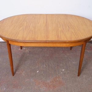 May include: An oval wooden dining table in light brown, with four tapered legs. The tabletop, with a visible wood grain, has a darker brown trim. The table's dimensions are approximately 150 cm in length and 90 cm in width.