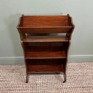 Puede incluir: Estantería de madera oscura con cuatro estantes y un diseño curvo. La estantería tiene una parte superior decorativa y descansa sobre patas curvas. Los estantes están espaciados uniformemente. Una pieza de mobiliario clásica, de unos 100 cm de altura.