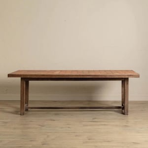 May include: A rectangular wooden table with a light brown surface and dark brown legs. The table has a simple, rustic design, with a long, flat top and four sturdy legs. The table is approximately 183 cm long and 91 cm wide.