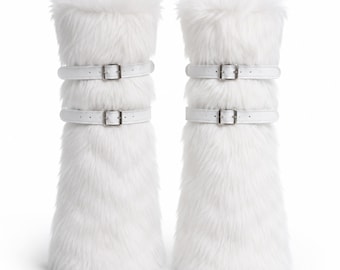 May include: A pair of white faux fur leg warmers featuring two horizontal straps with silver-toned metal buckles on each piece. The long, shaggy white synthetic fur covers the entire exterior, providing a textured appearance for these tall, cylindrical accessories.