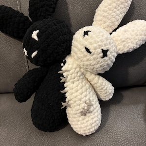 May include: A handmade crochet bunny in black and white. The black bunny has white stitched details, while the white bunny has black stitched details. The two bunnies are joined together, creating a unique plush toy.