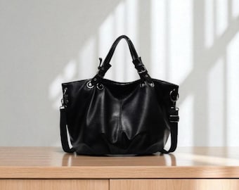 May include: A black tote bag with a shoulder strap and top handles. The bag is made of a smooth material and has silver-colored hardware. The bag is sitting on a wooden surface.