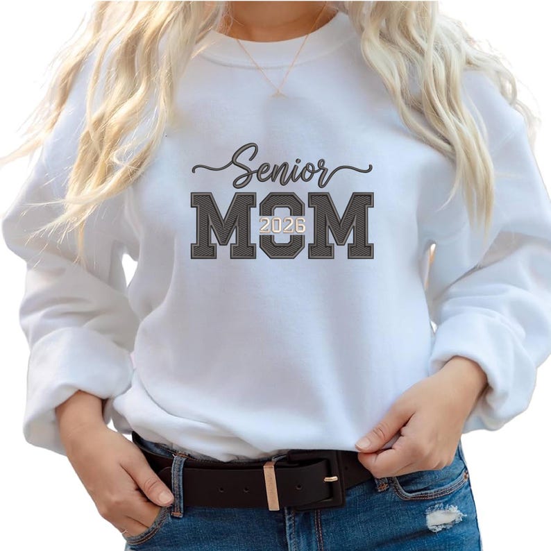 Puede incluir: Sudadera blanca con el texto "Senior MOM 2026" en negro y gris. La palabra "Senior" est&aacute; en cursiva, y "MOM" est&aacute; en letras de bloque. La sudadera tiene mangas largas y cuello redondo.
