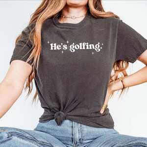 Comfort Colors® shirt he&#39;s golfing - shirt golfspeler voor moeder, vrouw golfer en cadeau golfende moeder, T-shirt golfliefhebber voor seizoen