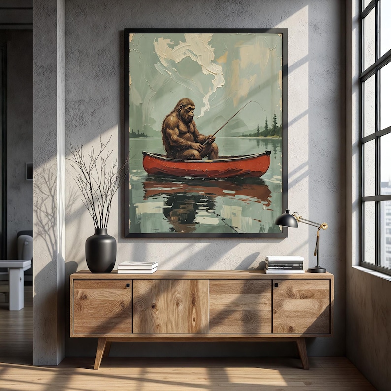 May include: A framed illustration of a large, brown, hairy figure sitting in a red canoe and fishing. The figure is wearing a red bandana and has a cigarette in its mouth. The canoe is floating on a blue lake with green trees in the background. The sky is blue with white clouds.