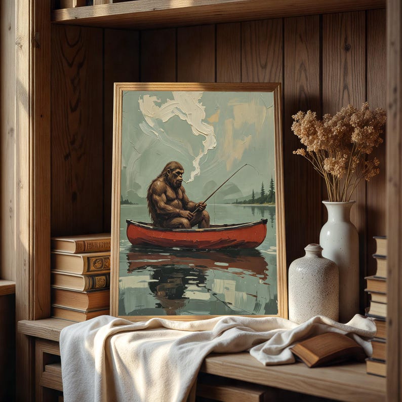 May include: A framed painting of a brown, hairy figure sitting in a red canoe on a lake. The figure is holding a fishing rod and is wearing a red bandana. The lake is surrounded by green trees and the sky is blue with white clouds.