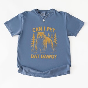 May include: A blue t-shirt with the text "CAN I PET DAT DAWG?" in yellow. The graphic features a bear and two trees. The shirt has short sleeves and a crew neck.