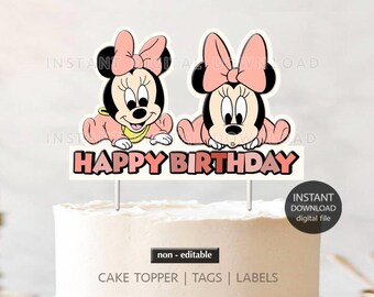 May include: A cake topper featuring two cartoon Minnie Mouse characters with pink bows and outfits. The words "HAPPY BIRTHDAY" are displayed below the characters. The cake topper is on top of a frosted cake.