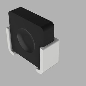 Op de afbeelding: Een zwart, vierkant object met een afgeronde bovenkant en een verzonken ovaal detail, vastgehouden in een witte, U-vormige houder. Het ontwerp is eenvoudig en modern, met een minimalistische esthetiek. De achtergrond is effen lichtgrijs.