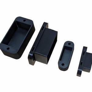 May include: Four black plastic components, possibly for an enclosure or project. Two larger pieces are rectangular with mounting holes. The smaller pieces are also rectangular with mounting features.