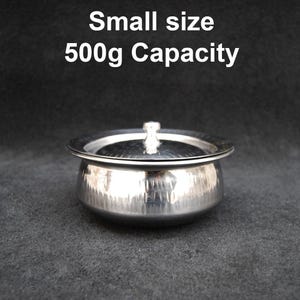 May include: A small, silver, stainless steel bowl with a lid. The bowl has a hammered finish and a capacity of 500g. "Small size 500g Capacity" is written in black text above the bowl.