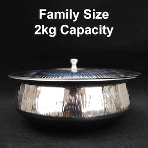 Puede incluir: Un bol de servir de acero inoxidable plateado con tapa. El bol tiene un acabado martillado y la tapa tiene un diseño estriado. El bol está etiquetado con "Family Size 2kg Capacity".
