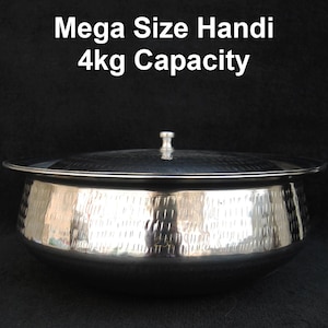 以下が含まれることがあります： 蓋付きの大きくて光沢のある銀色のハンディポット。ポットはハンマーで叩かれたような質感で、上部の「Mega Size Handi 4kg Capacity」というテキストで示されているように、4kgの容量があります。ハンディは調理と提供のために設計されています。