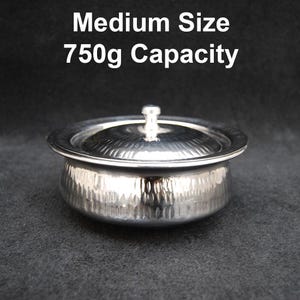 Puede incluir: Un tazón de acero inoxidable plateado con tapa. El tazón tiene un acabado martillado y una capacidad de 750 g.  Tamaño mediano 750 g de capacidad.