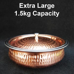 Puede incluir: Un cuenco de cobre extra grande con tapa. El cuenco tiene una textura martillada y un borde plateado. La tapa tiene un pequeño asa. El texto "Extra Large 1.5kg Capacity" se muestra encima del cuenco.