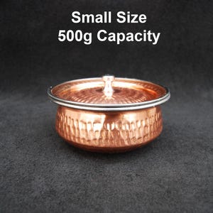 Puede incluir: Un pequeño cuenco de cobre martillado con tapa y borde plateado. La tapa tiene un pequeño asa. El texto "Small Size 500g Capacity" se muestra encima del cuenco. Capacidad de 500 gramos.