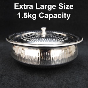 Puede incluir: Un bol de servir de acero inoxidable plateado con tapa. El bol tiene un acabado martillado y una capacidad de 1,5 kg. El texto "Extra Large Size 1.5kg Capacity" está impreso sobre el bol.