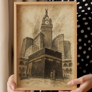 Pode incluir: Um esboço em tons sépia emoldurado da Kaaba em Meca, Arábia Saudita, com a torre do relógio ao fundo. A obra de arte está em uma moldura de madeira clara, segurada por uma pessoa vestindo um vestido de bolinhas pretas e brancas.